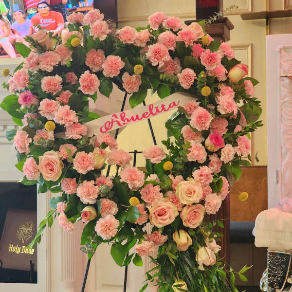 Large pink floral wreath on a stand with a name ribbon