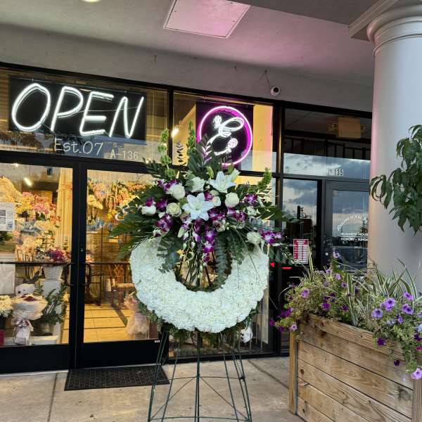 Large white floral wreath on a stand with white lilies and purple orchids