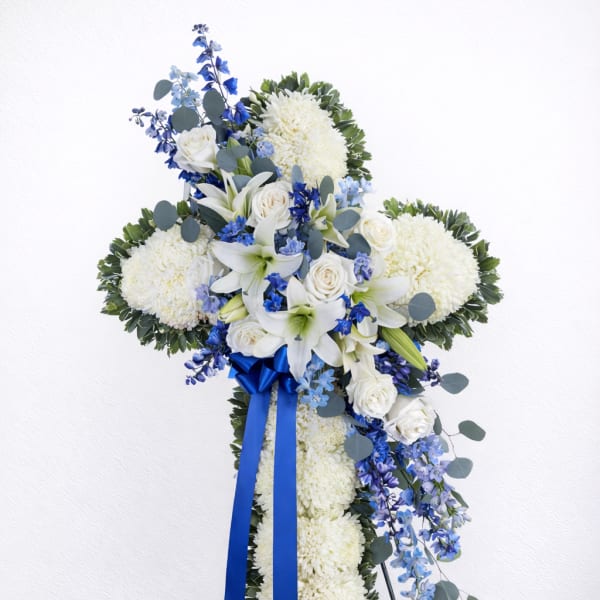 Standing floral cross with white blooms, blue flowers, and a blue ribbon
