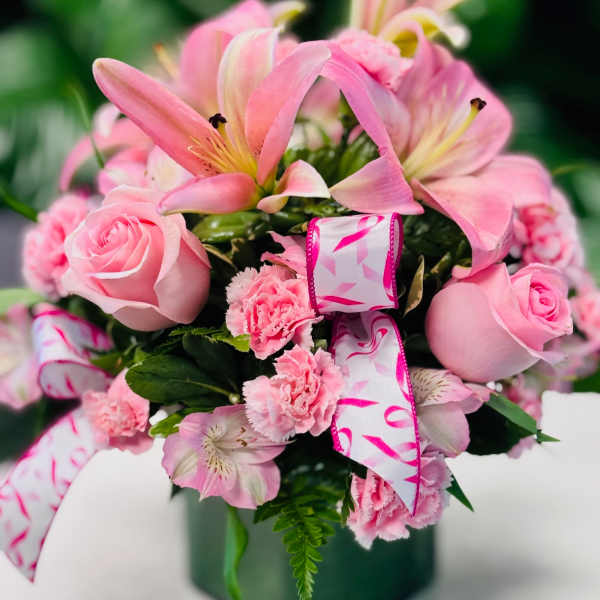 Pink lilies, roses, and carnations in a green vase with ribbon