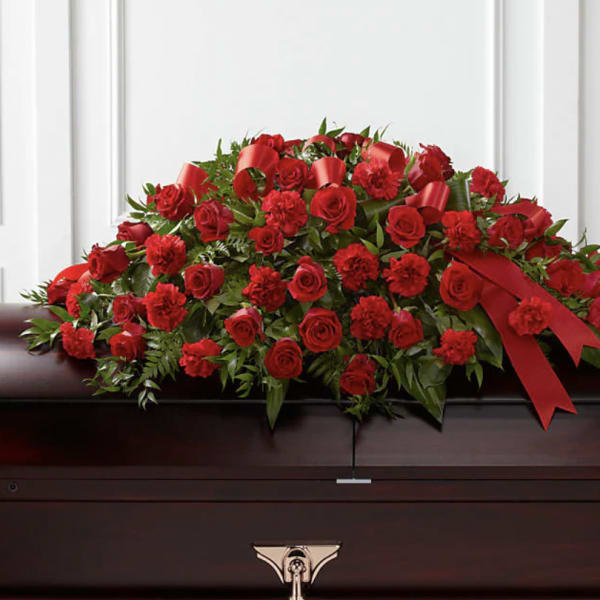 Red rose and carnation casket spray with ribbon on a dark casket