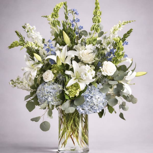 White lilies and blue flowers in a clear glass vase