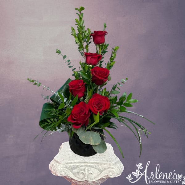 Tall arrangement of red roses in a black vase with greenery