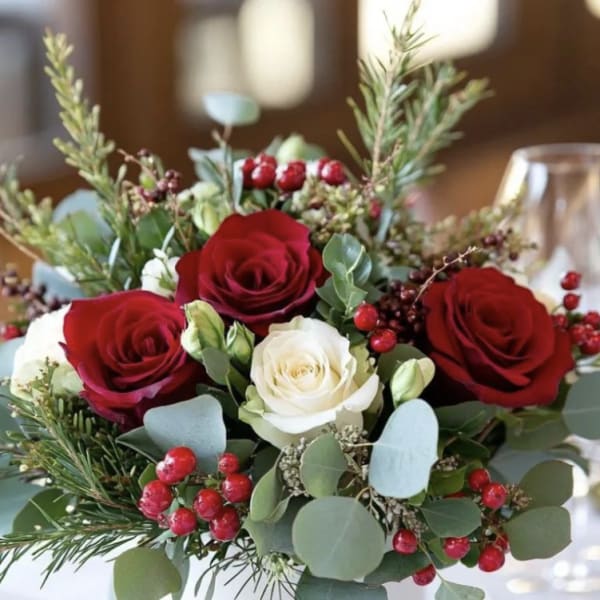 Red and white roses in a white vase with berries and greenery
