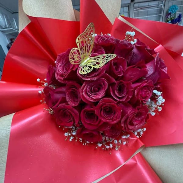 Bouquet of deep pink roses wrapped in bright red paper with a butterfly topper