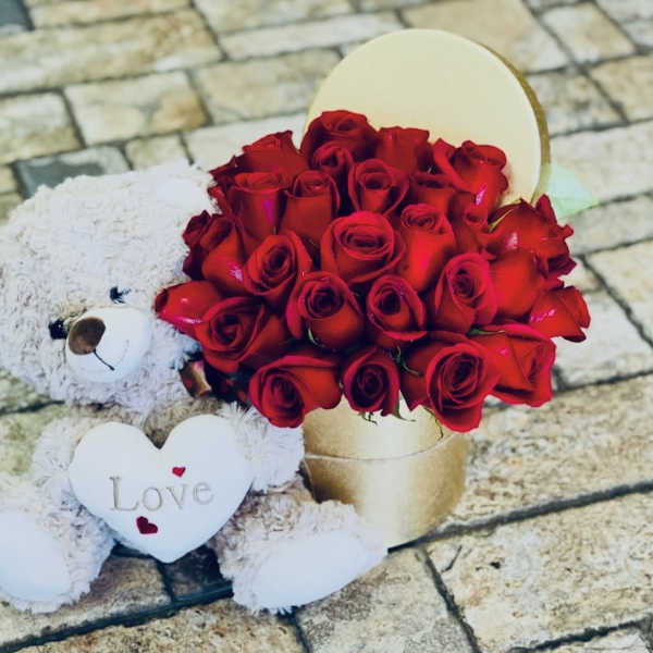White teddy bear beside a box of red roses with a heart that says Love