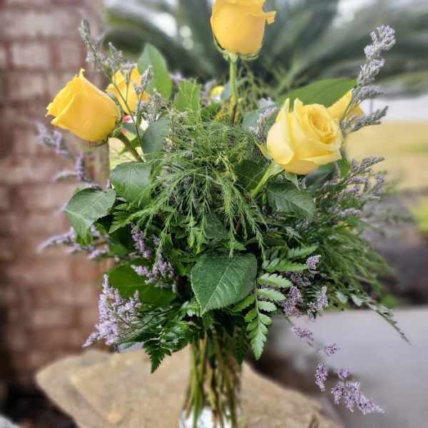 Yellow roses in a clear glass vase with mixed greenery