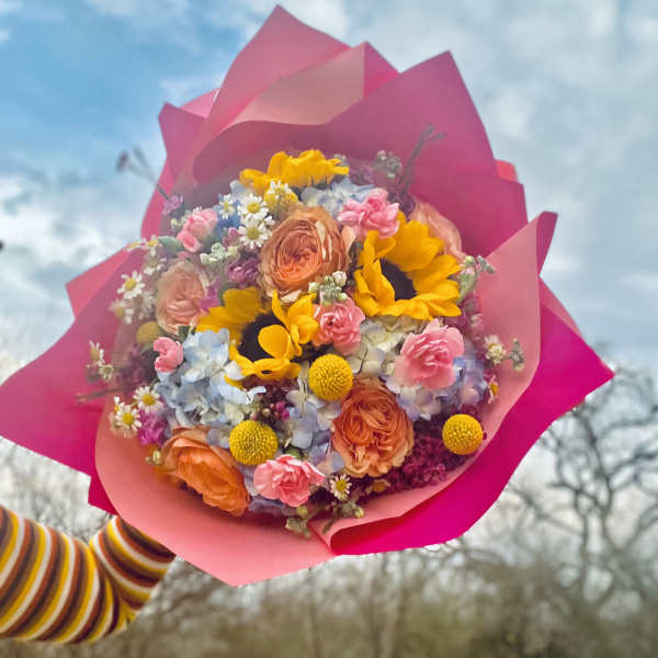 Colorful bouquet with sunflowers, roses, and small daisies wrapped in bright pink paper