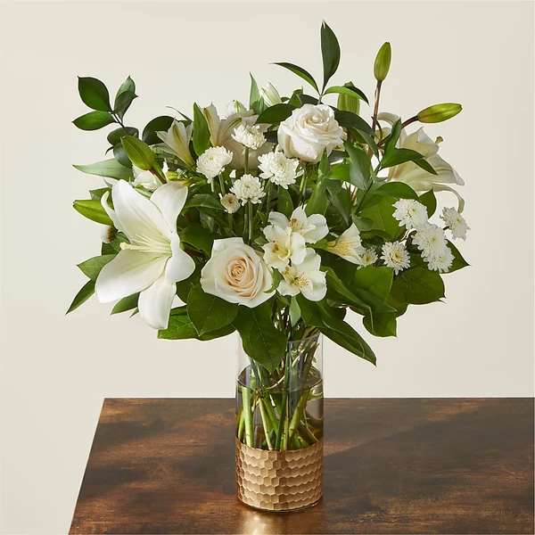 White lilies and roses in a glass vase with green foliage