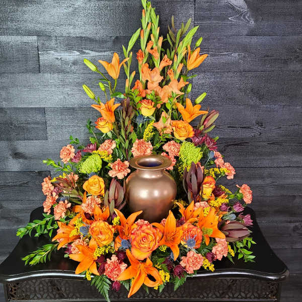 Orange lilies and roses arranged around a bronze urn centerpiece