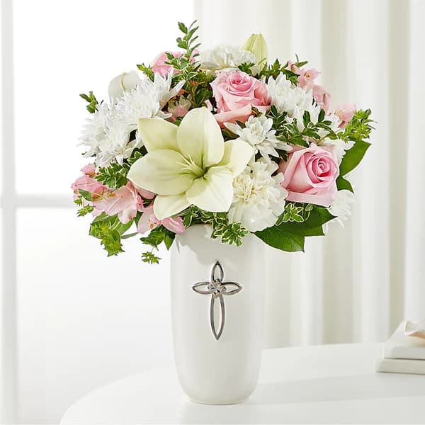 Pink roses and white flowers arranged in a white vase with a cross emblem