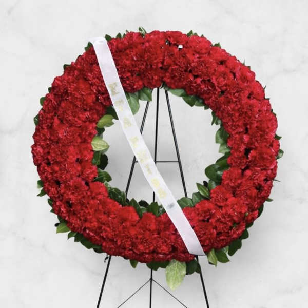 Red floral wreath on a black stand with a white ribbon