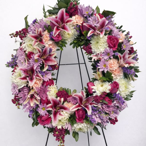 Large floral wreath with pink lilies, roses, and purple daisies on a stand
