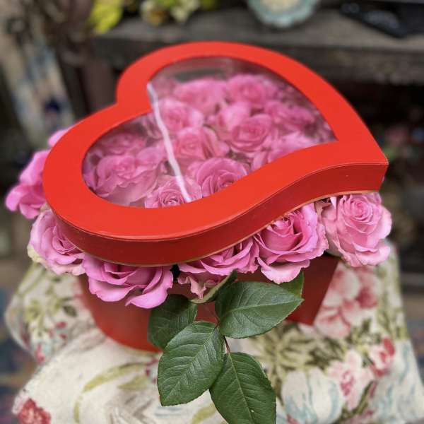 Pink roses in a red heart-shaped box with a clear lid