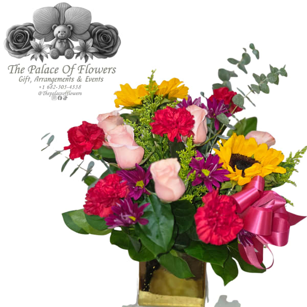 Mixed bouquet with roses, carnations, sunflowers, and purple daisies in a gold vase