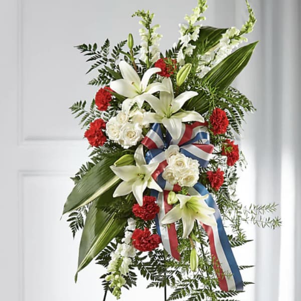 Standing floral spray with white lilies, red carnations, and ribbon on an easel