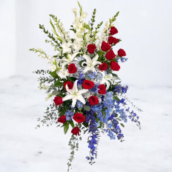 Tall floral spray with red roses, white lilies, and blue flowers