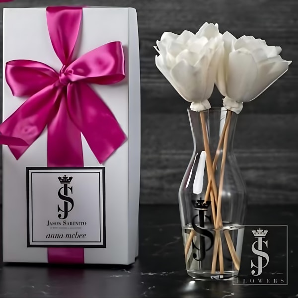 White flowers in a clear vase beside a gift box with a pink ribbon