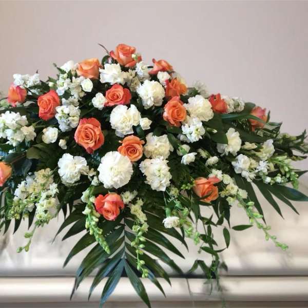 Orange and white floral casket spray with cascading greenery