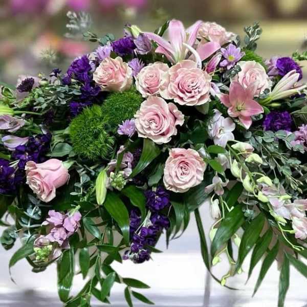 Low floral casket spray with pink roses and purple flowers