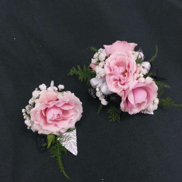 Two pink rose corsages with white baby's breath on a dark background