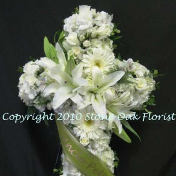 White floral cross arrangement with lilies and daisies on a black background