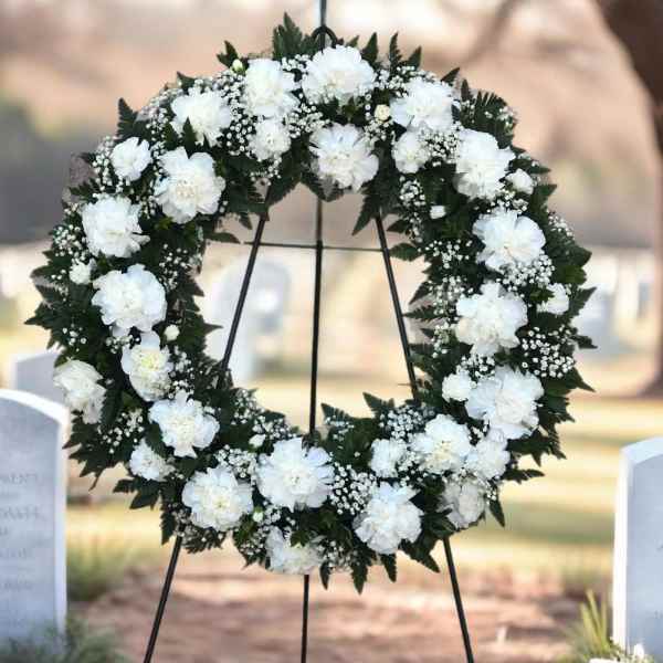 White floral wreath on a black stand at a gravesite