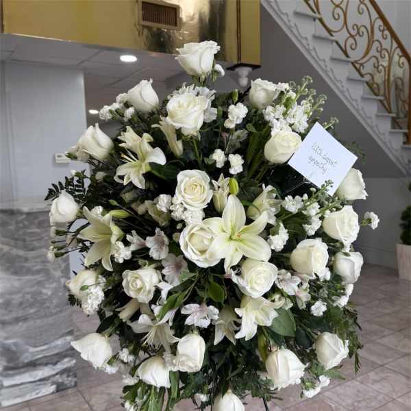 Large white sympathy standing spray with roses and lilies on an easel