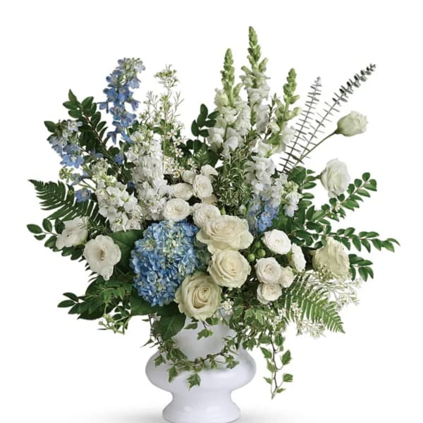 White and blue floral arrangement in a white urn vase