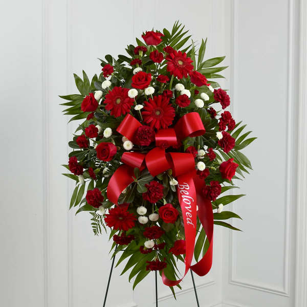 Red floral standing spray with a large red ribbon on a black easel