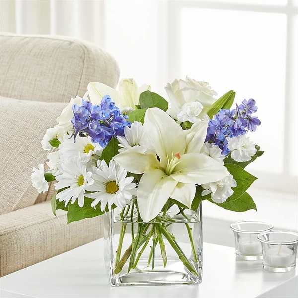 White lilies and daisies with blue flowers in a clear glass vase