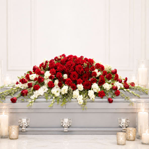Red and white floral casket spray with candles around it