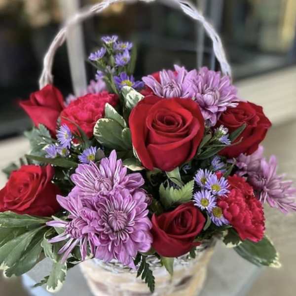 Basket of red roses and purple daisies with a white handle