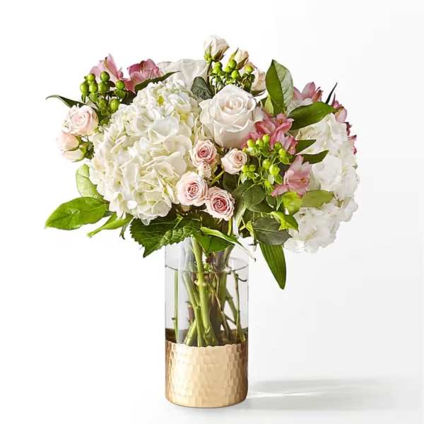 White and pink floral bouquet in a clear glass vase with a gold base