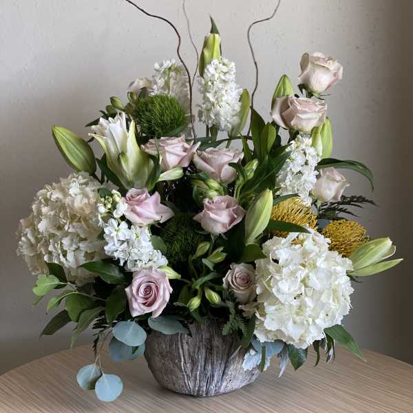 Arrangement of pale roses, white lilies, and hydrangeas in a rustic vase