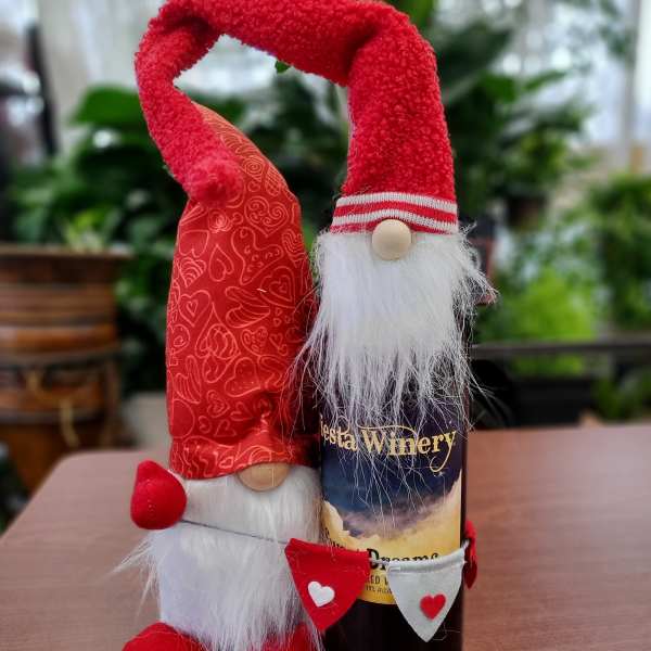 Two red gnome figurines stand beside a wine bottle on a table.