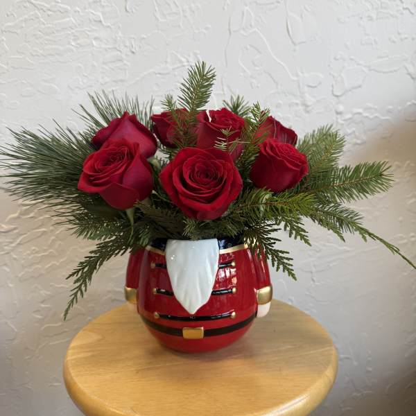 Red roses arranged in a Santa-shaped ceramic vase with evergreen branches
