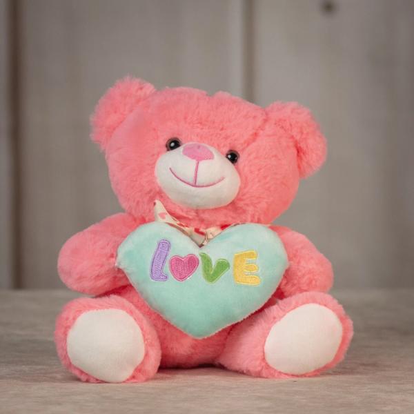 Pink teddy bear holding a mint heart pillow embroidered with the word love.