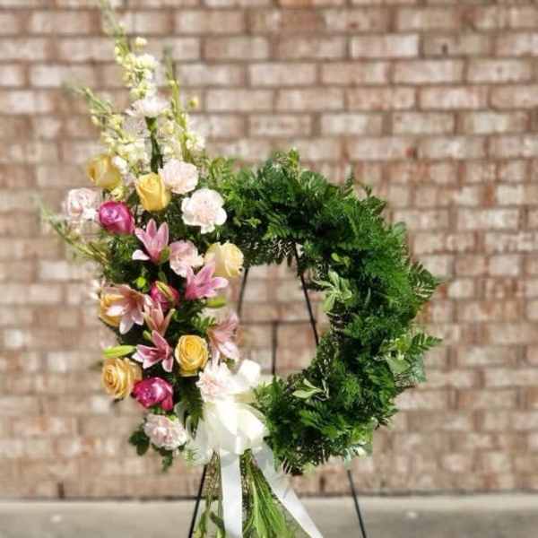 Floral wreath on a stand with pink, yellow, and white blooms