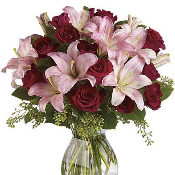 Arrangement of pink lilies and red roses in a clear glass vase
