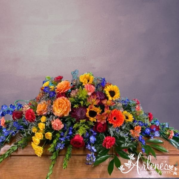 Colorful casket spray with roses, sunflowers, gerbera daisies, and blue flowers