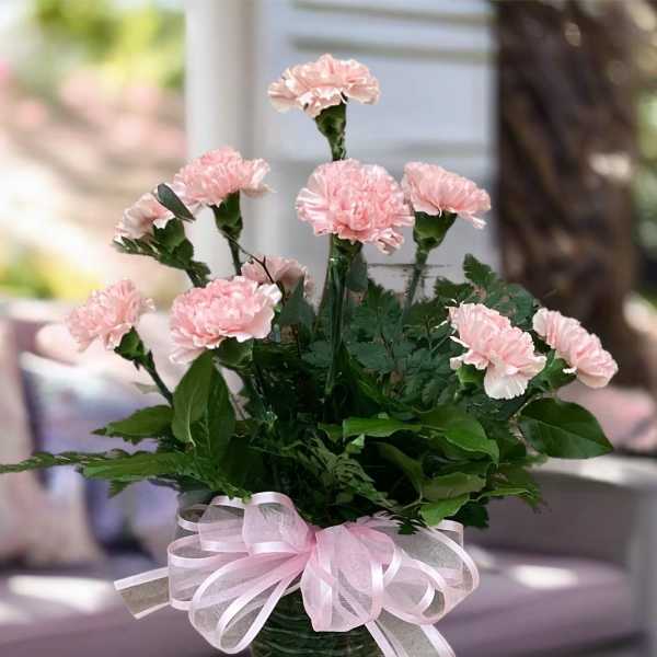 Pink carnations in a green glass vase with a pink ribbon bow