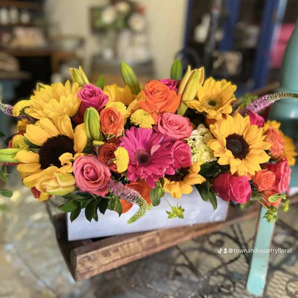 Bright mixed bouquet with sunflowers, roses, and lilies in a white container