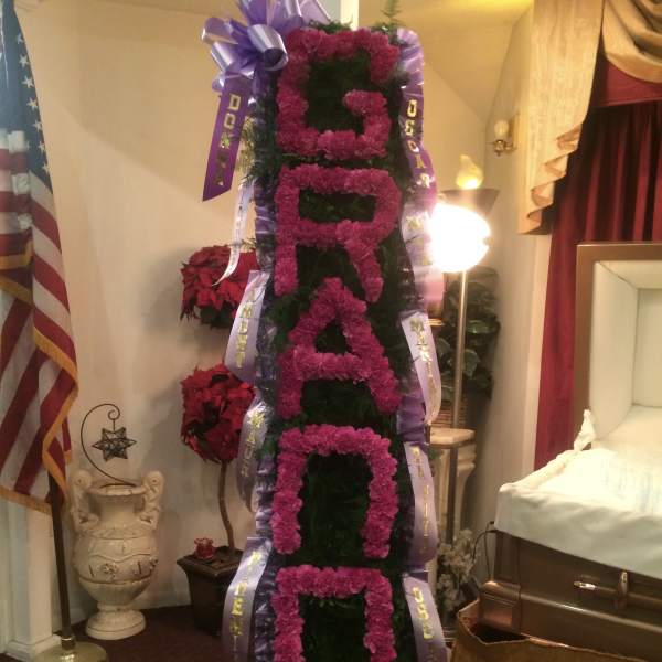 Tall funeral spray with pink flowers and purple ribbons in a room