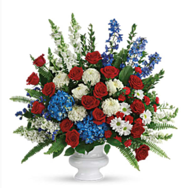 Large red, white, and blue flower arrangement in a white pedestal urn