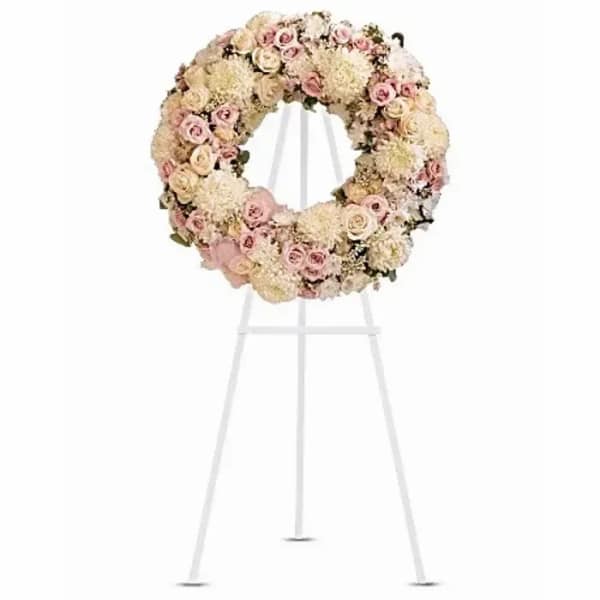 Round floral wreath on a white easel with pale pink and cream flowers