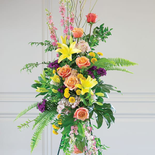 Tall floral standing arrangement with roses, lilies, and mixed blooms