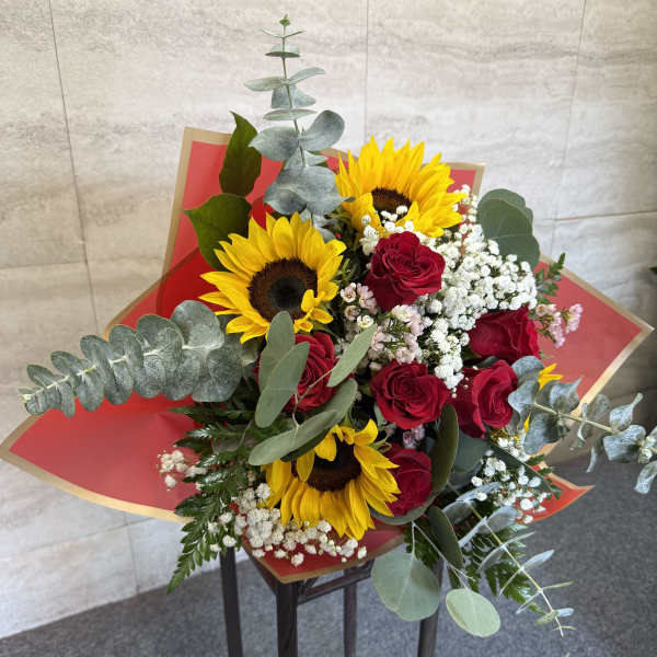 Bouquet of red roses and yellow sunflowers with white filler in red wrap