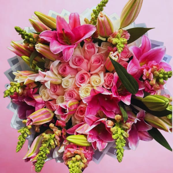 Bouquet of pink lilies and roses with green accents on a pink background