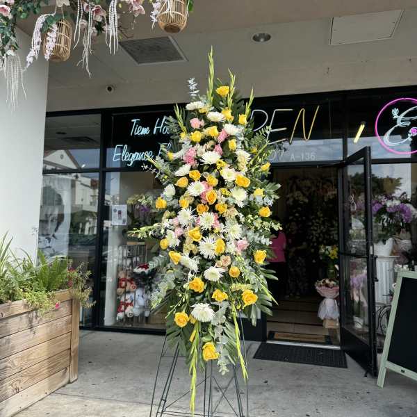Tall standing floral spray with yellow and white blooms on a metal easel